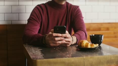 man using phone in a cafe with breakfast