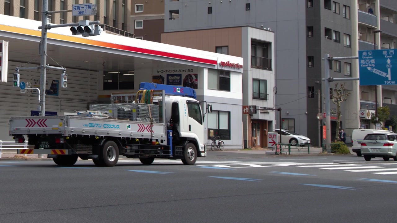 東京の広い都市の交差点を日中に車とトラックが走行する。
