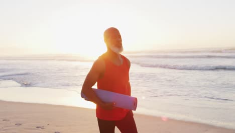 Älterer-Afroamerikanischer-Mann,-Der-Mit-Yogamatte-Am-Strand-Spaziert