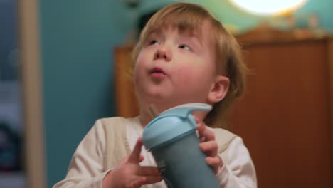 a handsome baby boy drinking smoothie from a blue drinking container and looking up to his parents - close up