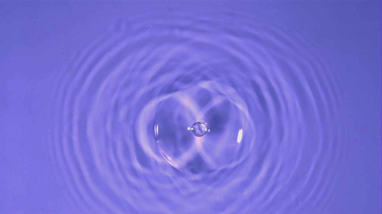 Vanddråbe i slow motion, der skaber ringe på lilla baggrund