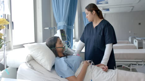 diverse female patient in hospital bed and female doctor giving her oxygen, copy space, slow motion