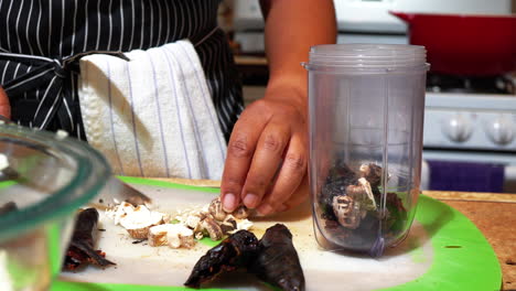mujer afroamericana corta champiñones en un recipiente de licuadora con pimientos secos