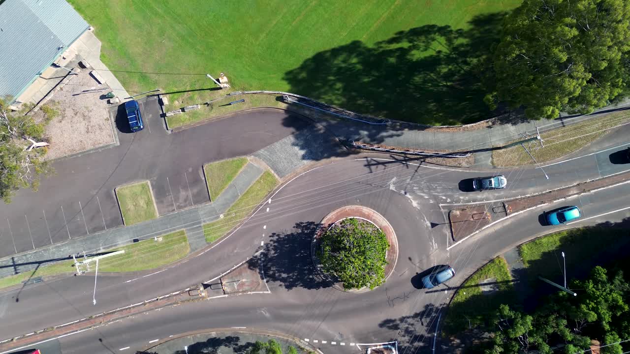 Drone aerial landscape of truck and car vehicles driving through roundabout on suburban town street surrounded by bushland trees and community oval in Killarney Vale Central Coast Australia transport