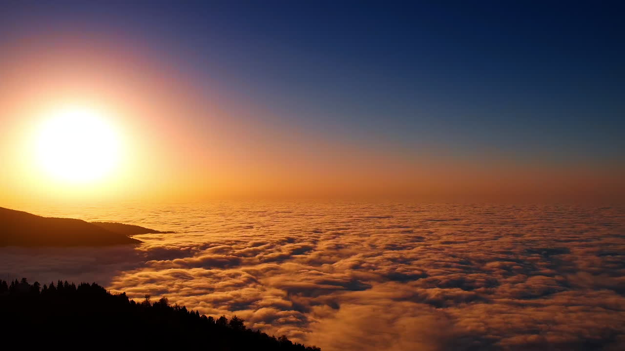 La puesta de sol tiñe el denso paisaje de nubes cubriendo el escenario entre las montañas. Silueta oscura de la roca sobresaliendo de las nubes. Vista aérea