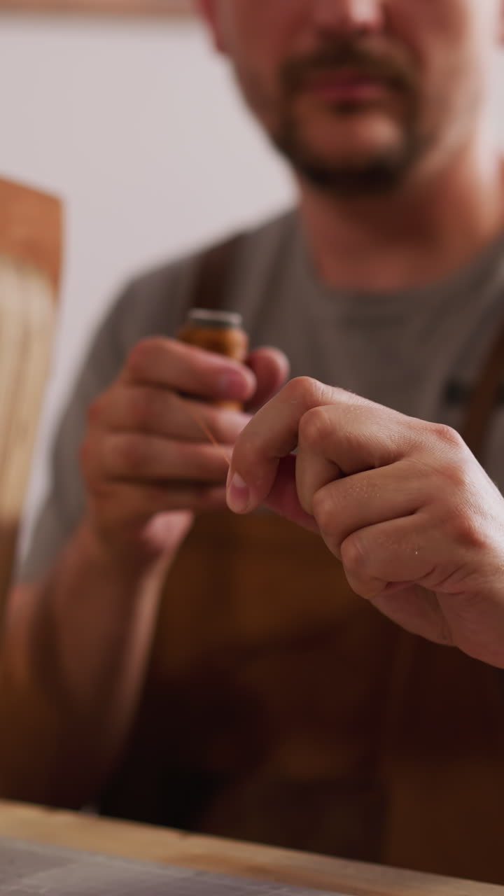 Master unrolls waxed thread for leather items sewing in craft workshop closeup. Traditional tools for handcraft and manufacturing selective focus