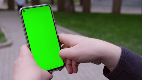 point of view of woman at street sitting on a bench using phone with green mock-up screen chroma key.