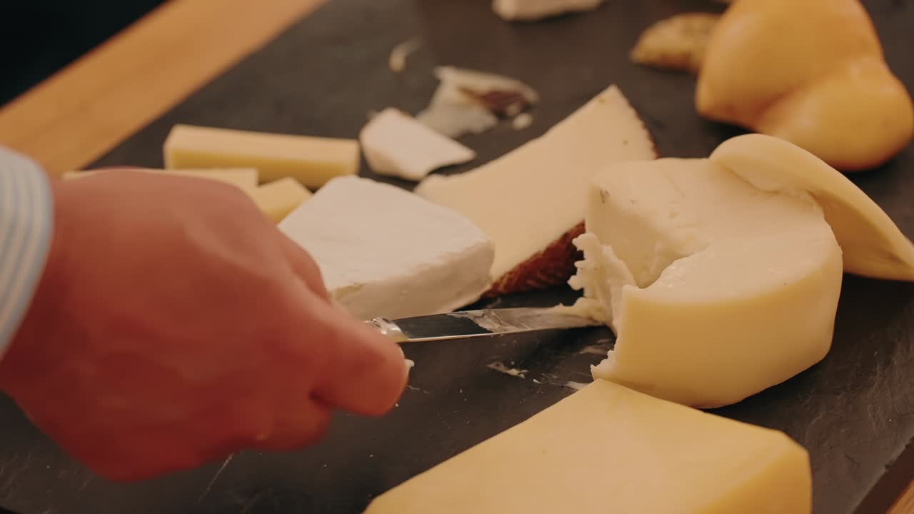 hand slicing creamy artisan cheese on elegant dark board