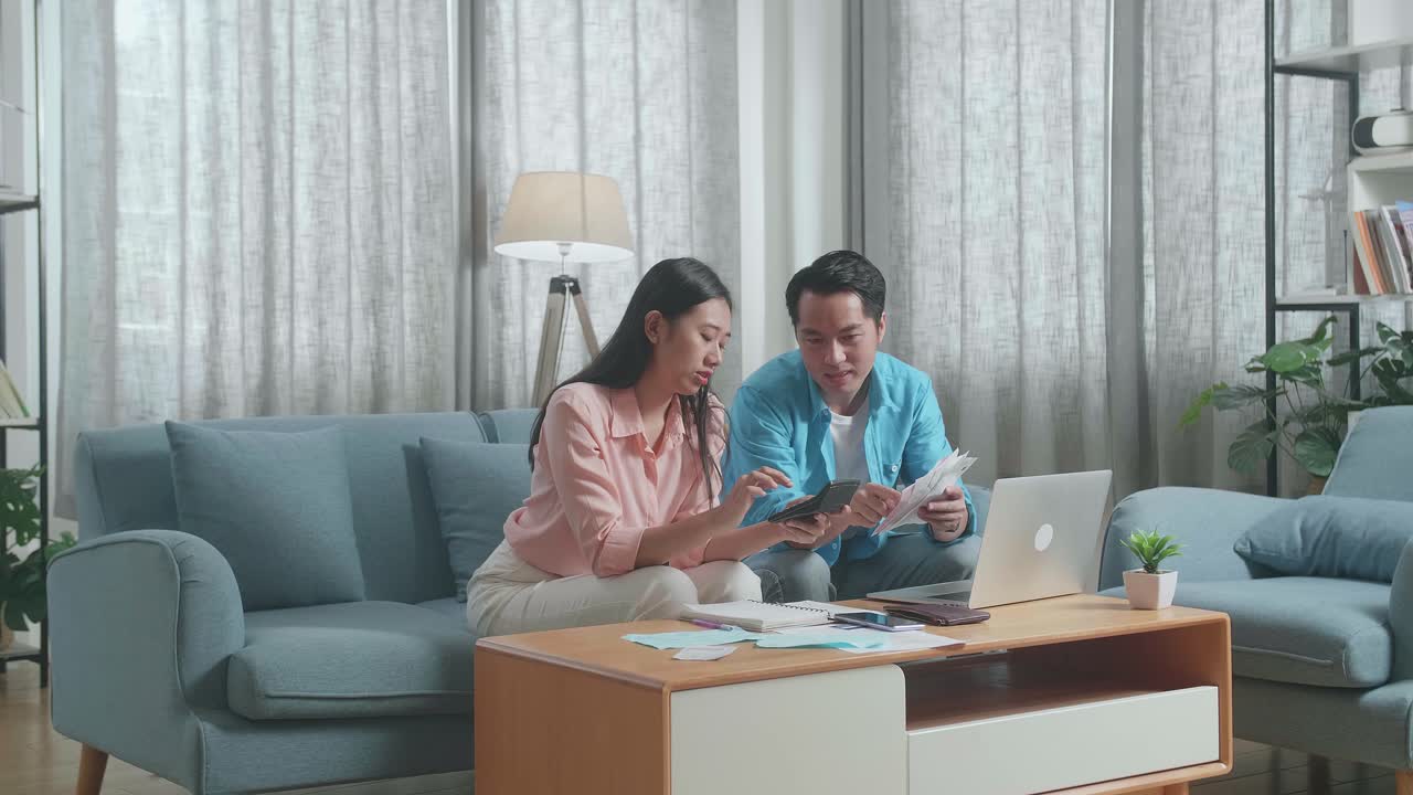 ラップトップを持ったアジア人カップルが互いにカリキュレーターでお金を計算するのを手伝った後頭痛を感じています