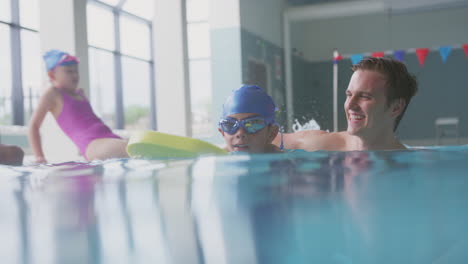 male swimming coach giving boy holding float lesson in pool