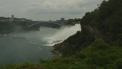 wide scenic shot of niagara falls, featuring the rainbow bridge, a balloon ride in the sky, and the mist rising from the crashing water below
