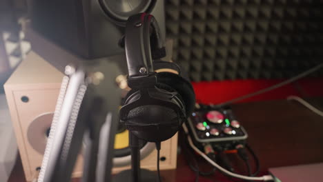 close-up of a studio setup featuring a speaker, headphones, and a blurred sound mixer in the background. emphasizing the tools of sound production with a focus on the speaker and headphones