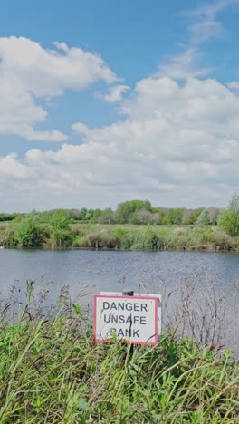 public warning sign on riverbank reads 'danger unsafe bank' vertical shot