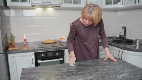 woman thoroughly cleans countertop with rag in modern kitchen, ensuring hygiene and tidiness, kitchen equipment neatly arranged in background