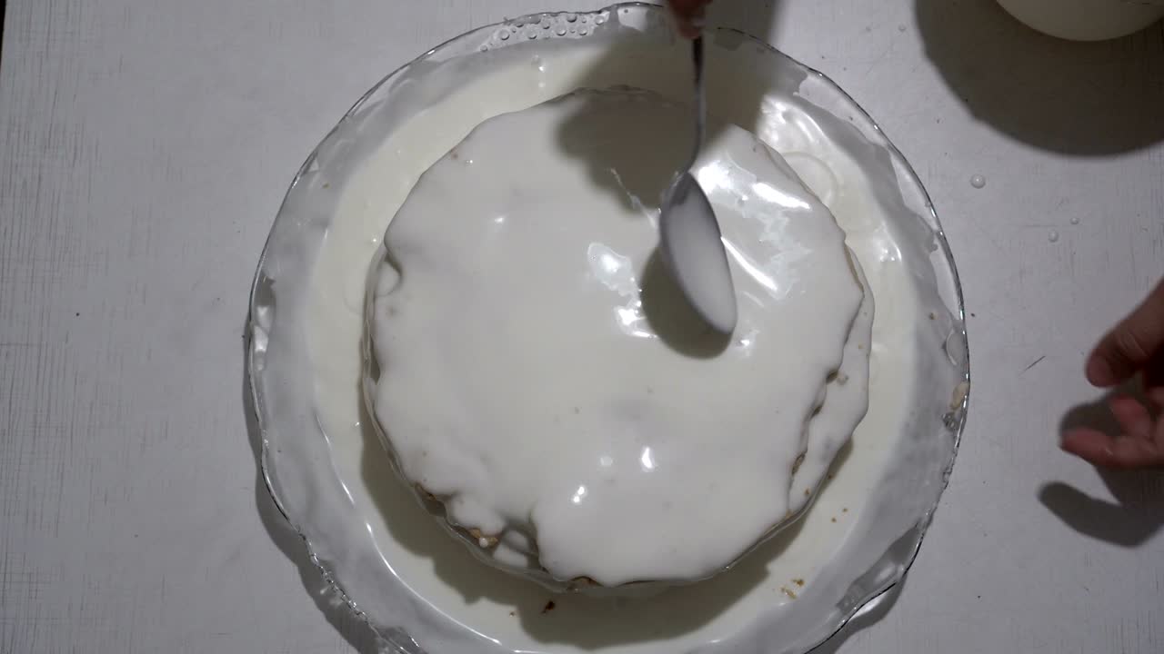 девушка готовит торт и наливает его белым сливком и шоколадом. она смазывает его на поверхность торта. приготовление сладкого десерта. вид сверху. 4к.