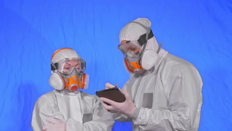 scientist virologist in respirator makes write in an tablet computer with stylus. man and woman wearing protective medical mask. chroma key blue.