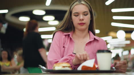 woman seated in restaurant takes a potato chip, bites it, closes eyes in satisfaction, and shakes head while enjoying the flavor, bright restaurant lights illuminate the background