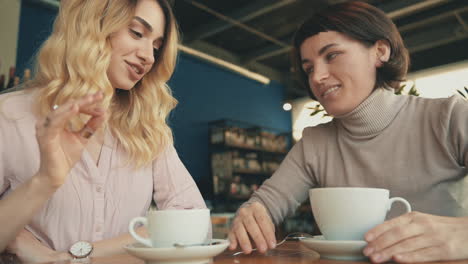 Blonde-And-Brunette-Female-Friends-Sharing-Moments-And-Talking-In-A-Coffee-Shop