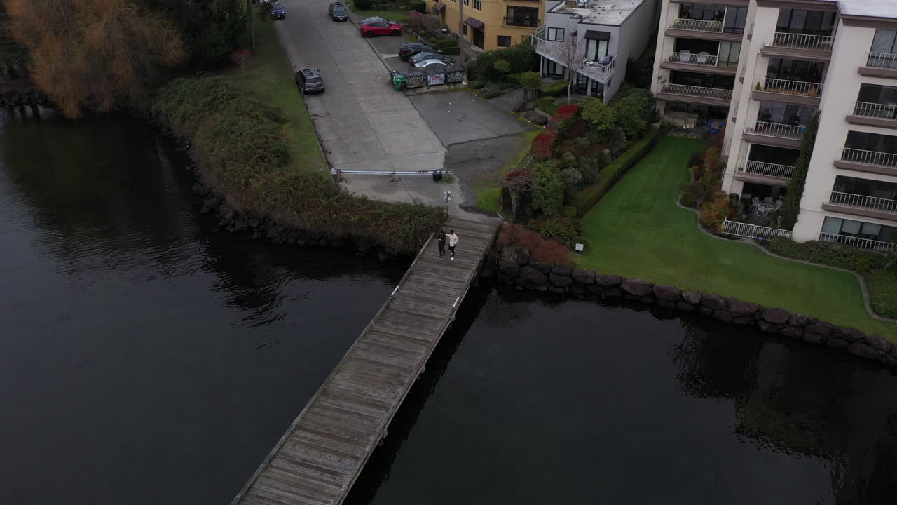 Drone view of a couple walking over a dark water pier in the morning