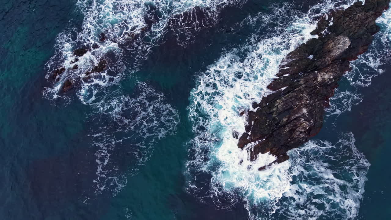Waves crashing against rocky coastline at sunset, creating a vibrant splash of white foam in a tranquil sea