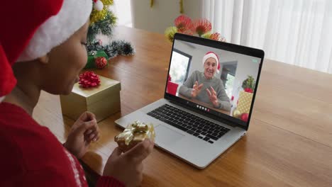 Afroamerikanische-Frau-Mit-Weihnachtsmütze-Nutzt-Laptop-Für-Weihnachtsvideoanruf,-Mit-Mann-Auf-Dem-Bildschirm