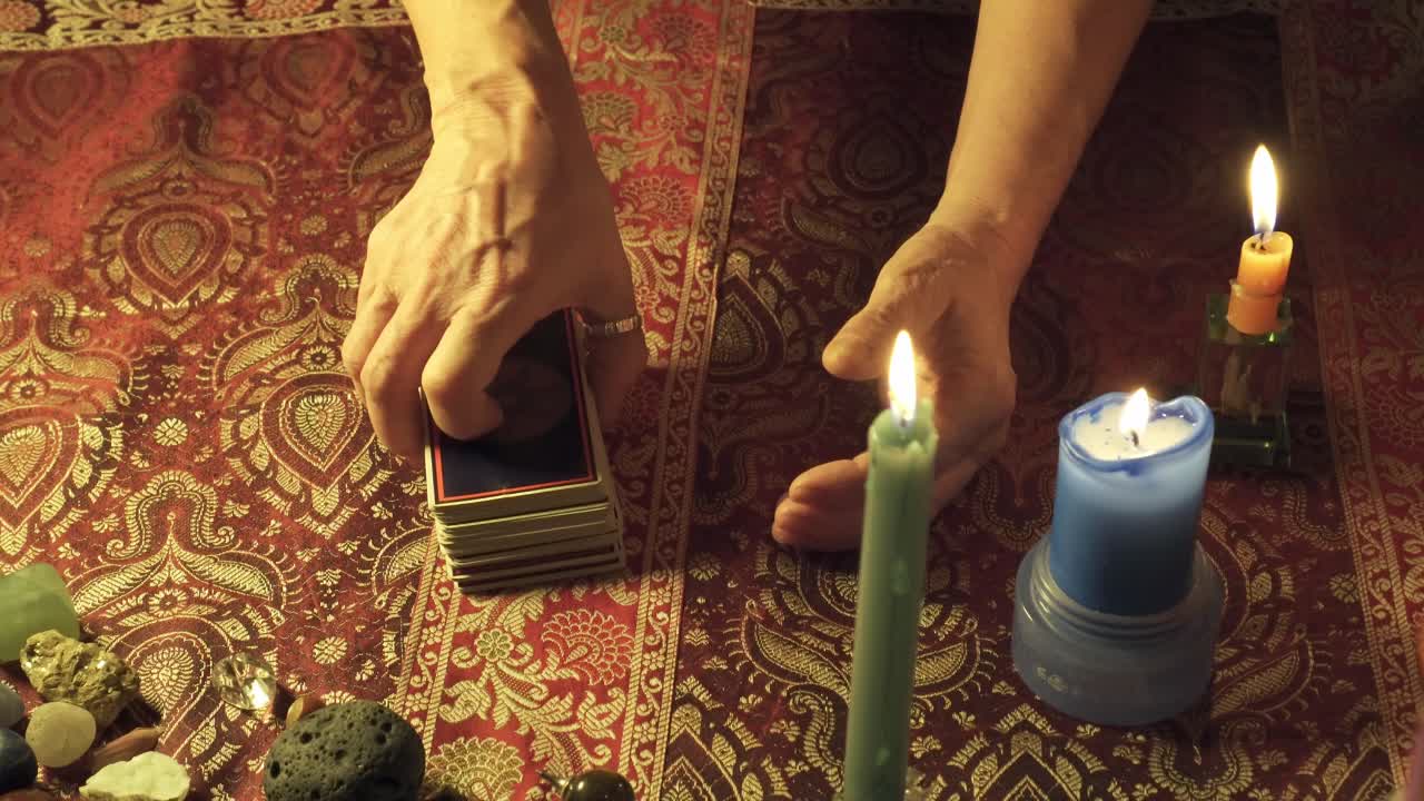 Close-up of a real tarot reader's hands predicting the future with tarot cards on a mystical table with candles and gems