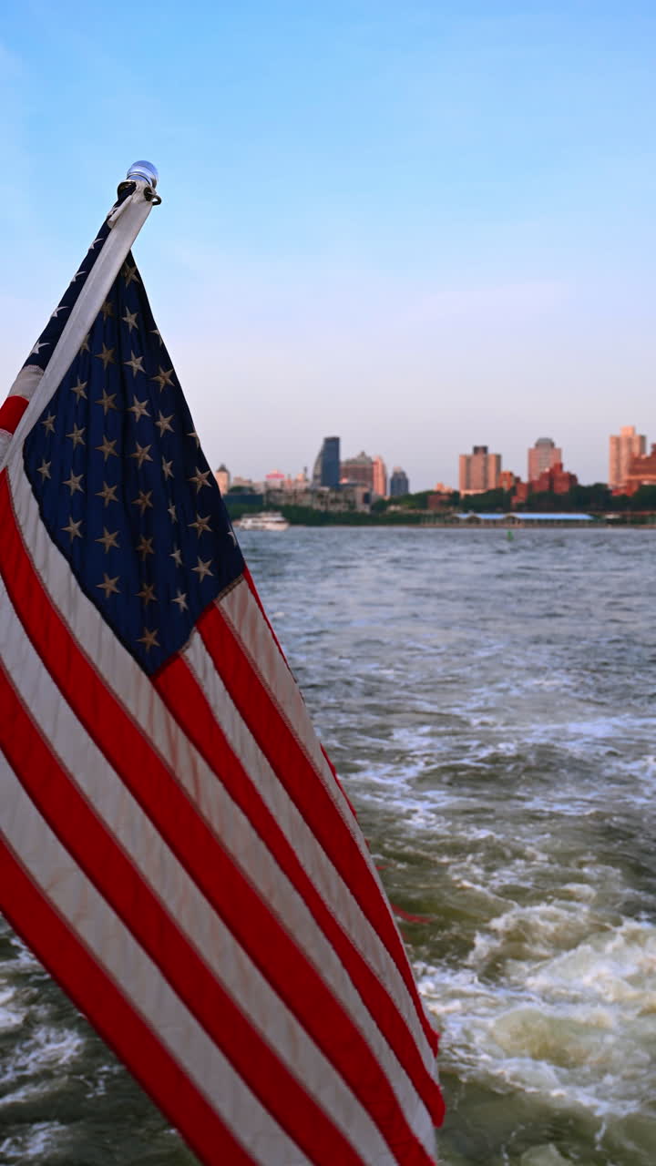 Bandiera americana sopra la scia del fiume e i ponti. Bandiera americana su un traghetto con scia schiumosa che conduce verso i ponti di New York in lontananza