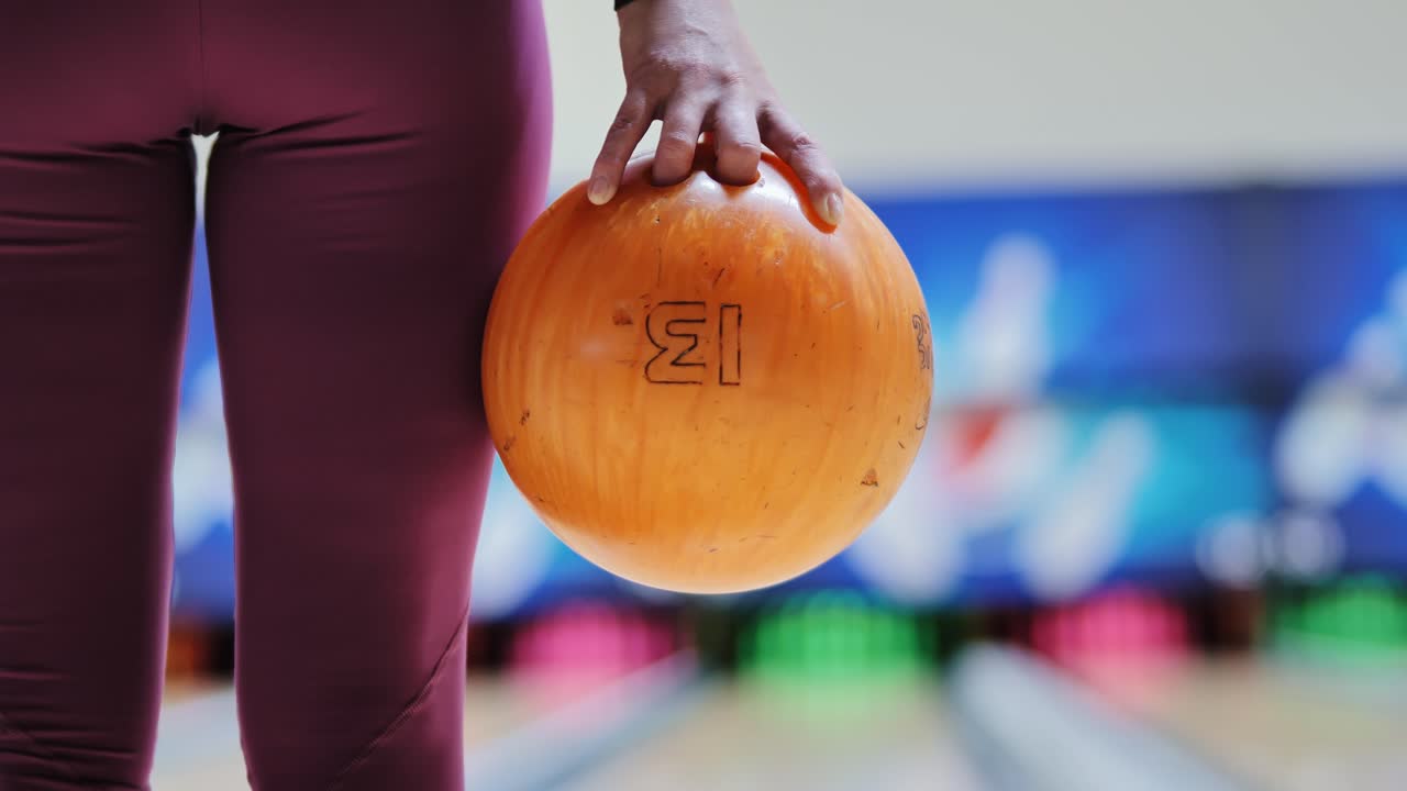 Tight frame showing woman hand holding orange ball before throw in bowling lane