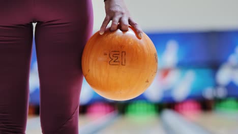 tight frame showing woman hand holding orange ball before throw in bowling lane