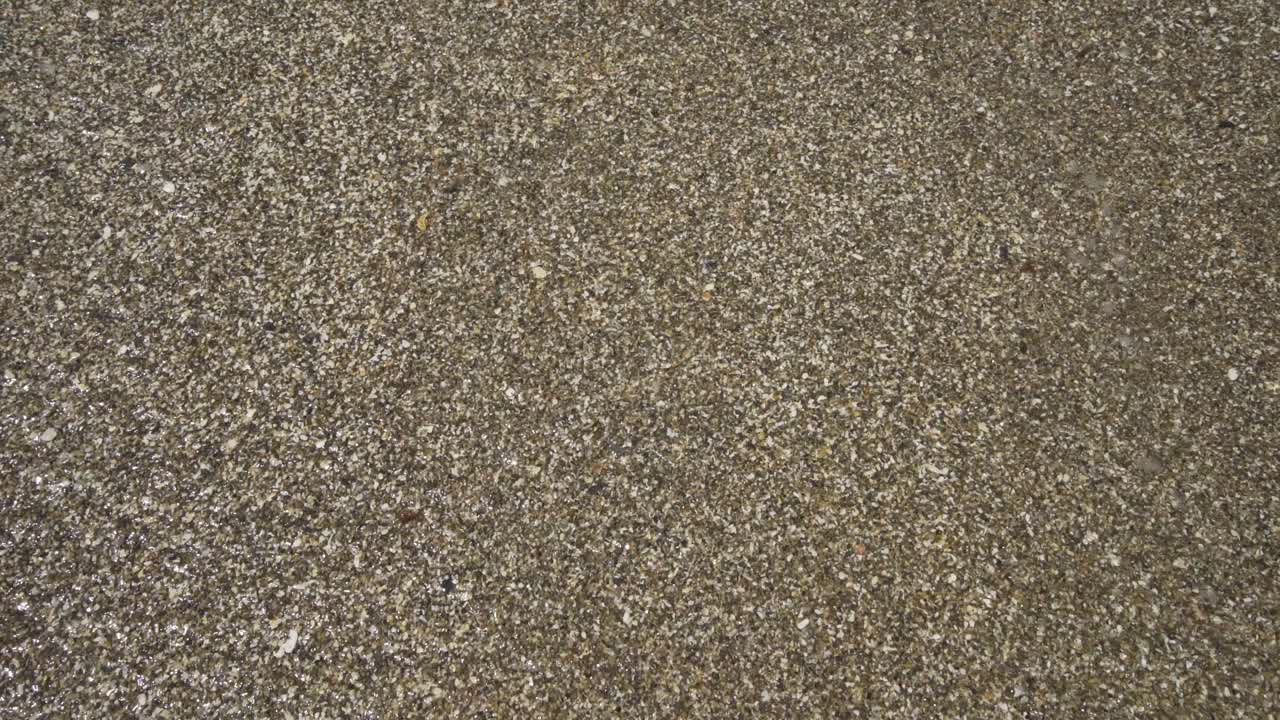 Gentle waves wash in and out across the grainy sand on the sunny beach of Cala de Mijas.