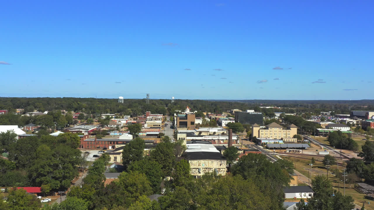 The drone retreats backwards over Tupelo, Mississippi, revealing the town's historic buildings, streets, and greenery under vast, sunny skies, unfolding the town's quaint charm