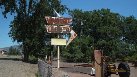 Walking-along-a-chained-link-fence-in-front-of-a-rusty-retro-lumber-store-sign-and-vintage-tractor-on-an-abandoned-road