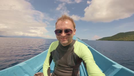 Ein-Fröhlicher-Mann-Mit-Sonnenbrille-Und-Neoprenanzug-Genießt-Eine-Bootsfahrt-Auf-Einem-Ruhigen,-Weiten-Meer