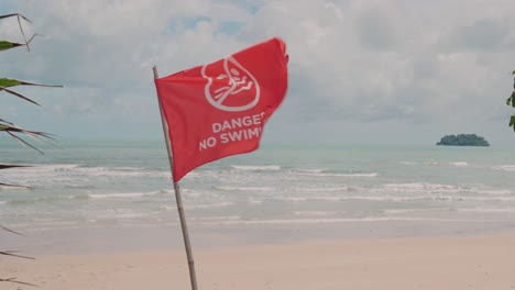 no swimming red flag bloowing in the wind at tropical beach, horizon over water