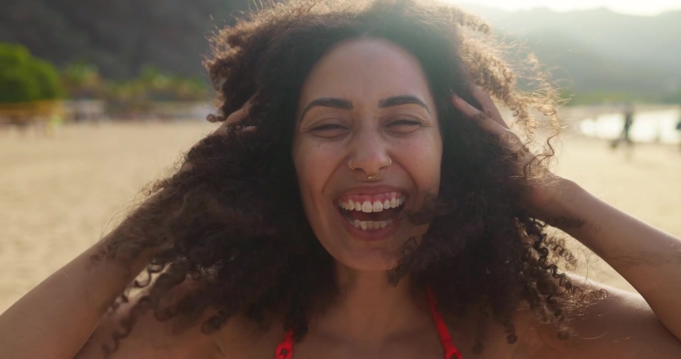 Ritratto ravvicinato di una giovane donna felice con i capelli ricci che ride sulla spiaggia.