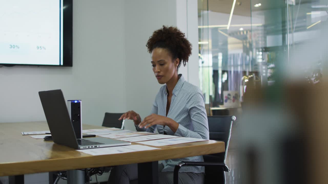 Mixed race businesswoman sitting at desk, checking documents and using laptop in office