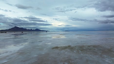 wide aerial drone dolly in rising shot of the famous bonneville salt flats in utah near wendover, nevada flooded from rain, creating mirage reflections with mountains on a stormy spring evening