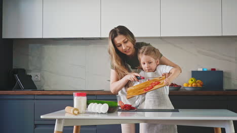 mother and girl put tomato slices into glass bowl at table