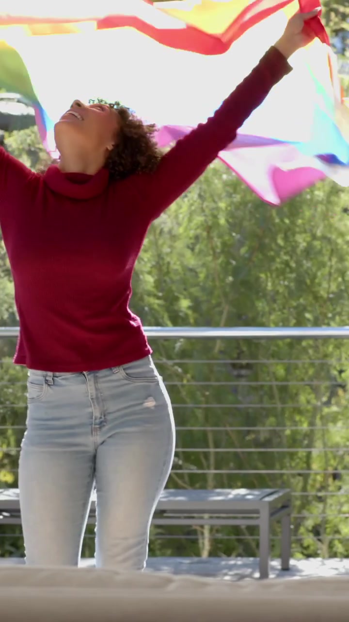 Video vertical: Mujer sosteniendo bandera del orgullo en la barandilla de la terraza, desplegándola y preparándola para la celebración del orgullo