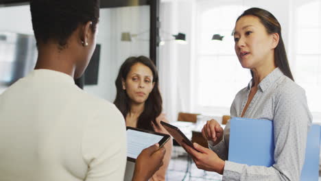 diverse businesswomen using tablets and talking in casual office meeting