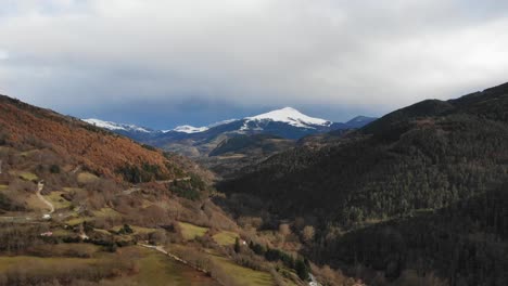 aerial: valley with a road with little traffic and a train track in a mountainous landscape with snow covered mountains in the background