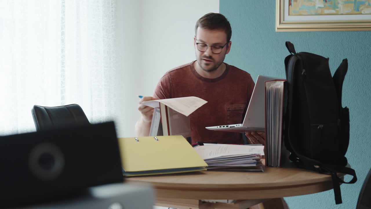 A man smiles during a video call at his home office, surrounded by folders and paperwork—likely using AI tools for support in study, finance, or legal tasks