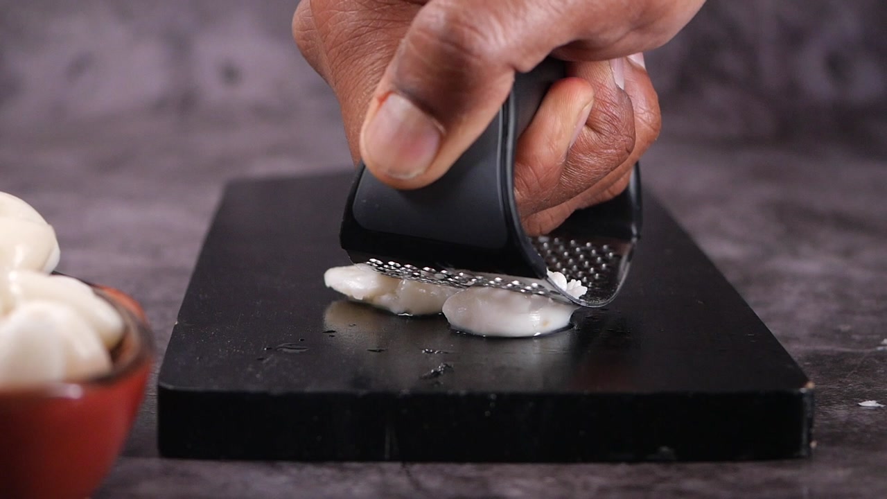 Close-up of hand crushing garlic cloves with a press