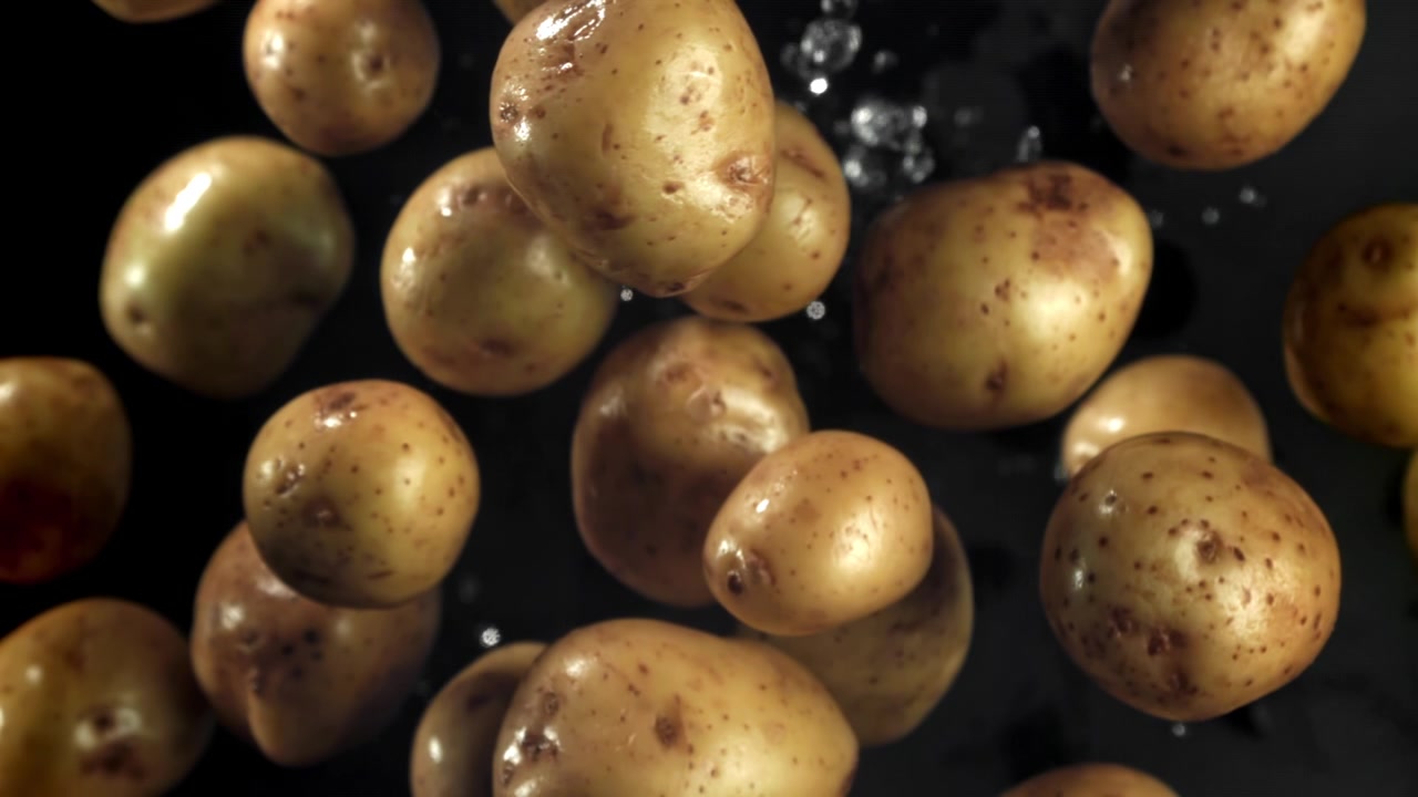 Patate crude galleggianti con goccioline d'acqua su sfondo scuro