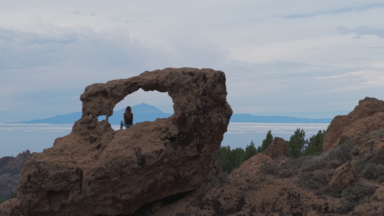 Timeless Beauty: The Window of Roque Nublo (Gañifa). Drone shot of a woman peacefully admiring the rugged peaks of Teide. Gran Canaria, Canary Islands.