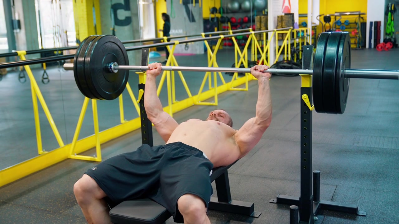 Hombre musculoso realizando press de banca con barra en un gimnasio