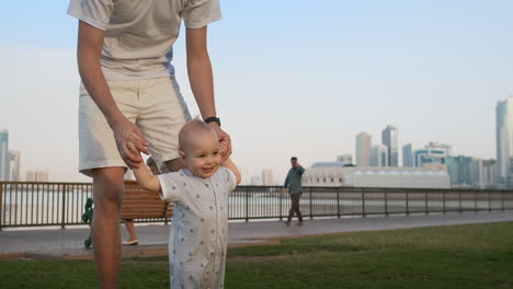 Padre-Joven-Con-Un-Niño-Y-Primeros-Pasos.-Padre-Joven-Con-Un-Niño-En-El-Aprendizaje-Al-Aire-Libre-Para-Dar-Los-Primeros-Pasos-Cerca-De-Una-Casa-Urbana-En-La-Ciudad