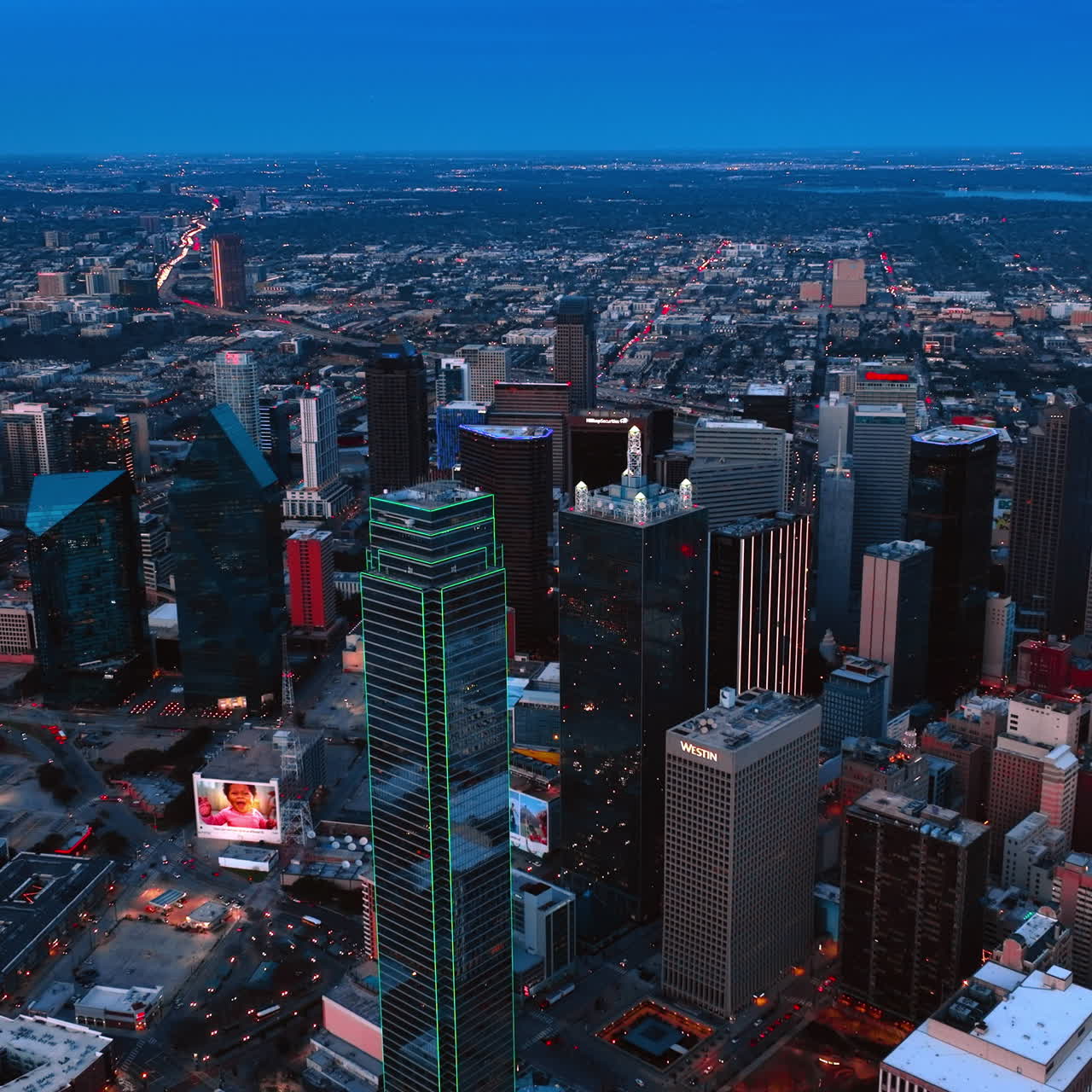 Il centro di Dallas con l'edificio Bank of America illuminato di verde al centro. Vasto panorama della metropoli al crepuscolo dall'alto.