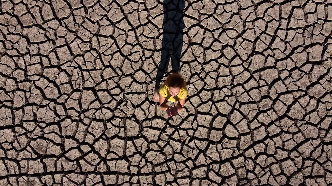 한 소녀가 하늘을 바라보며 가뭄 동안 건조하고 갈라진 흙 위에 서서 비를 기원합니다