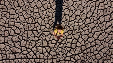 a girl looks to the sky and prays for rain whiloe standing on dry and cracked dirt during a drought